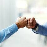 Close up of unrecognizable male entrepreneurs congratulating each other with fist bump in the office. Copy space.